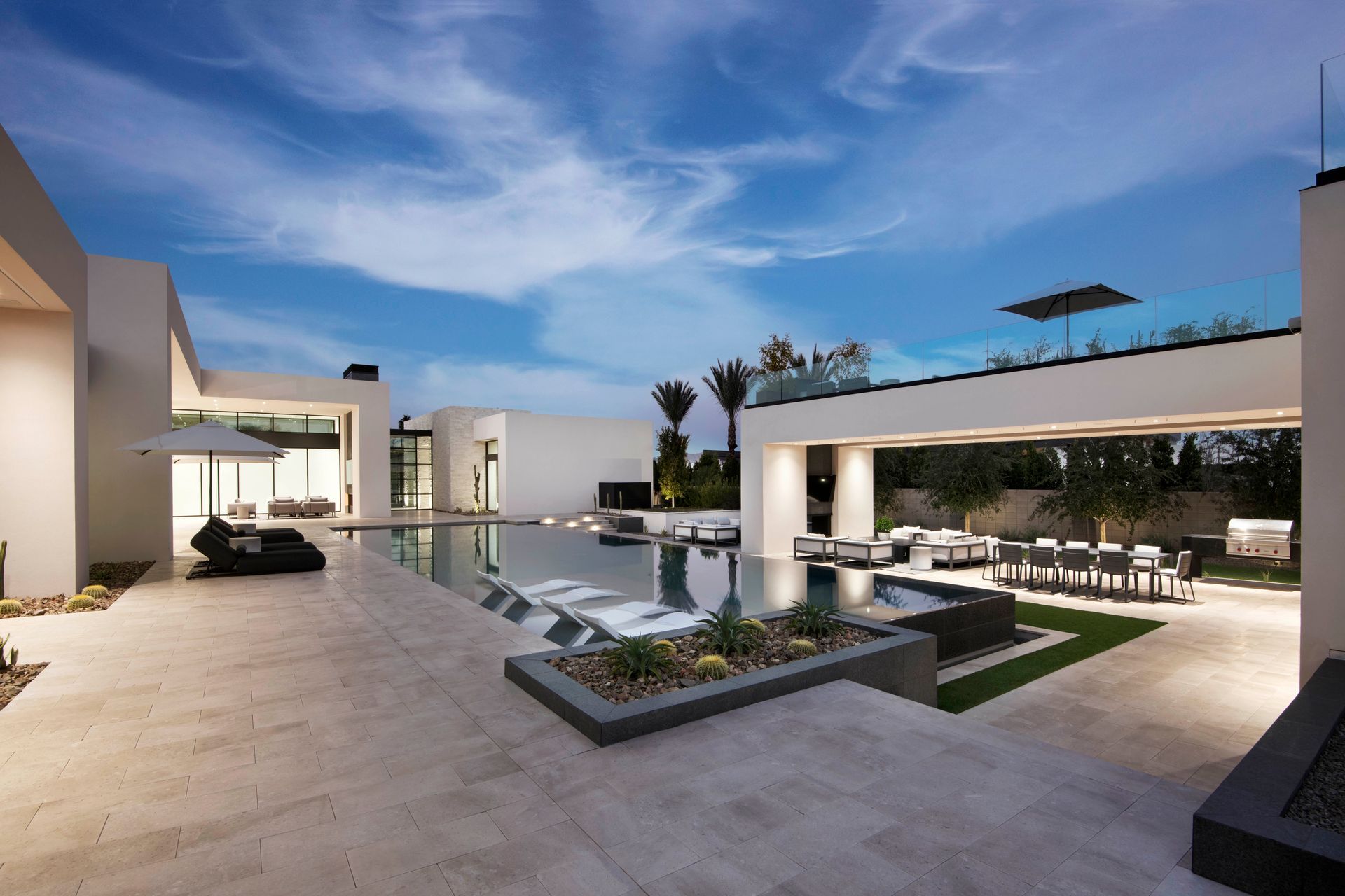 Modern luxury home exterior with pool, patio, and outdoor dining under a twilight sky.