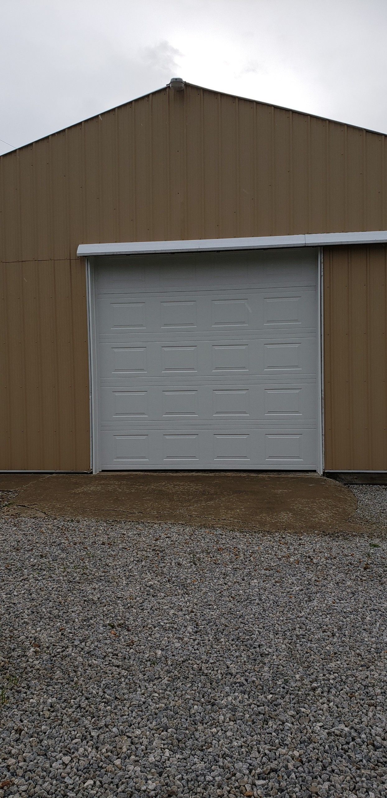 A brown building with a white garage door and gravel in front of it.