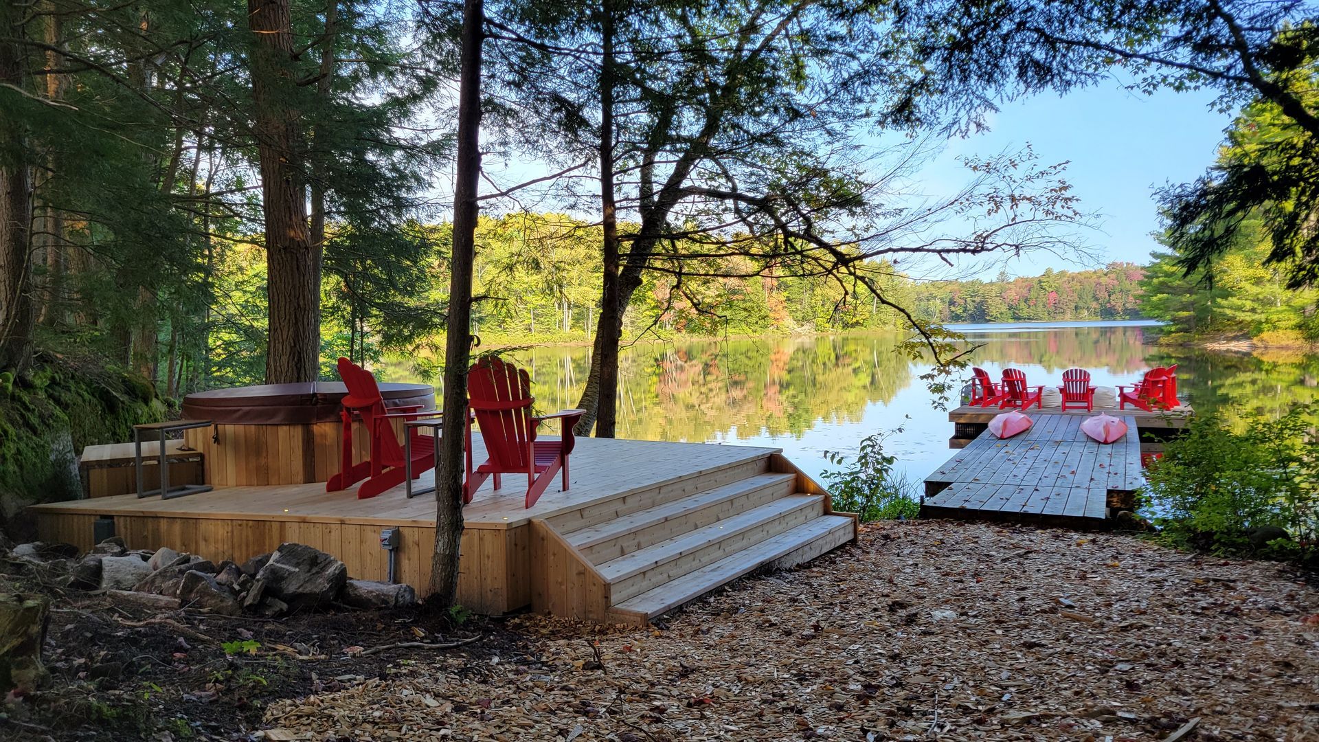 A wooden deck with red chairs and a hot tub next to a lake.