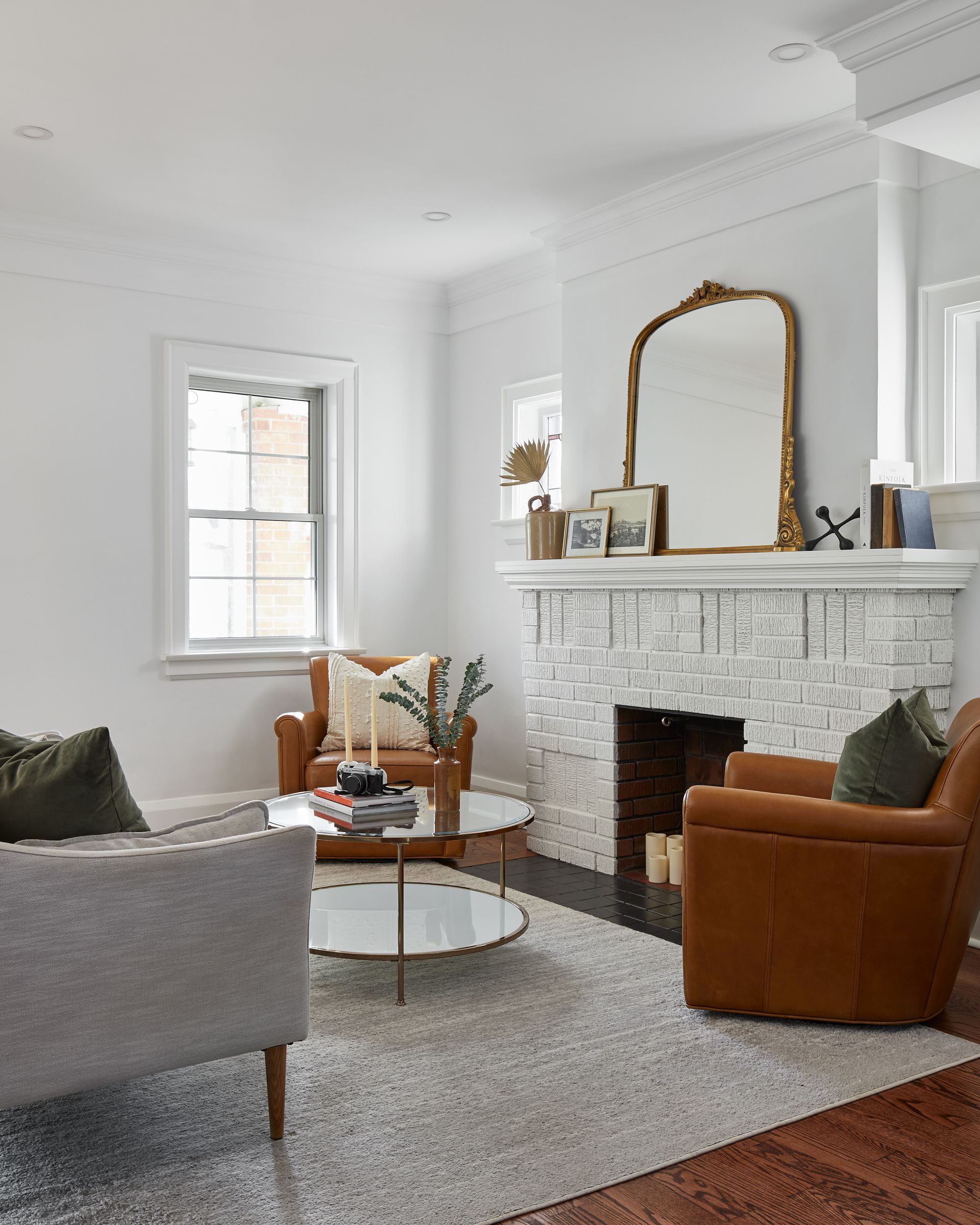 A living room with a fireplace , two chairs , a couch and a mirror.