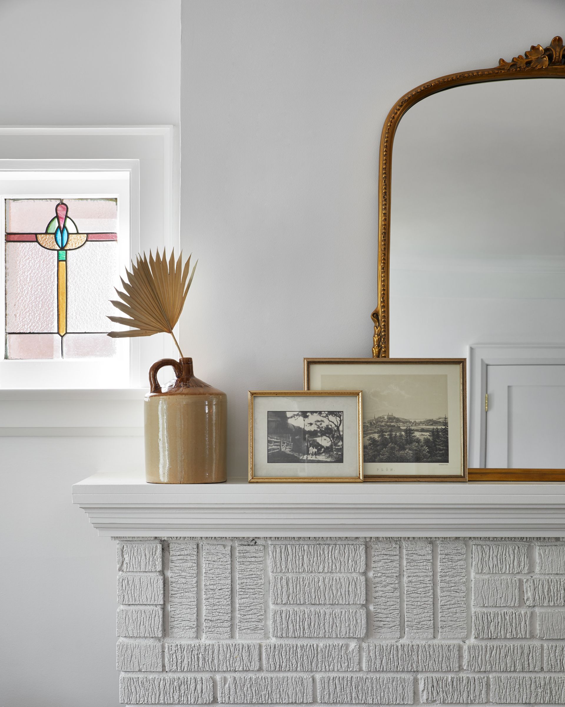 A fireplace with a vase , pictures , and a mirror on it.