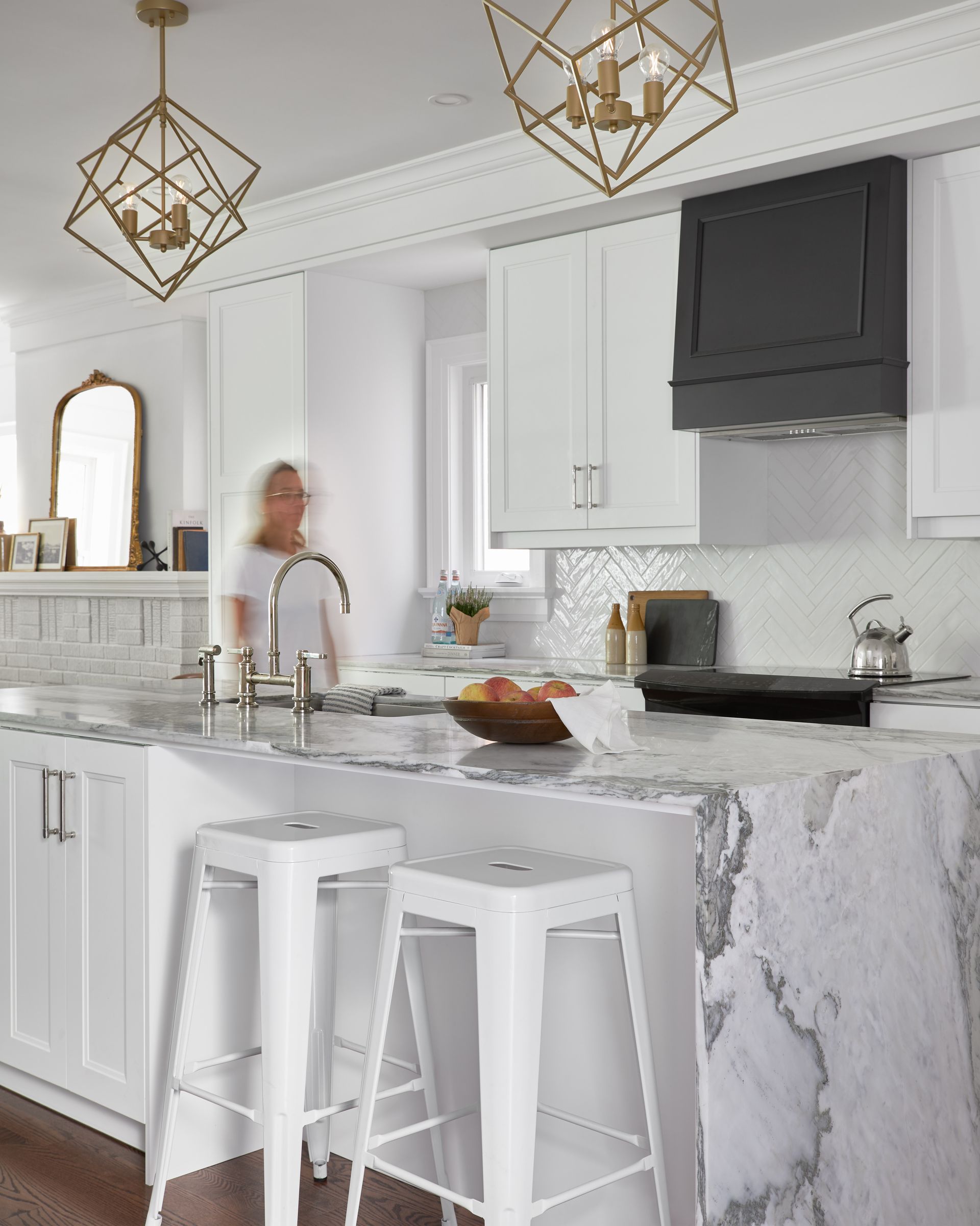 A woman is standing in a kitchen with white cabinets and marble counter tops.