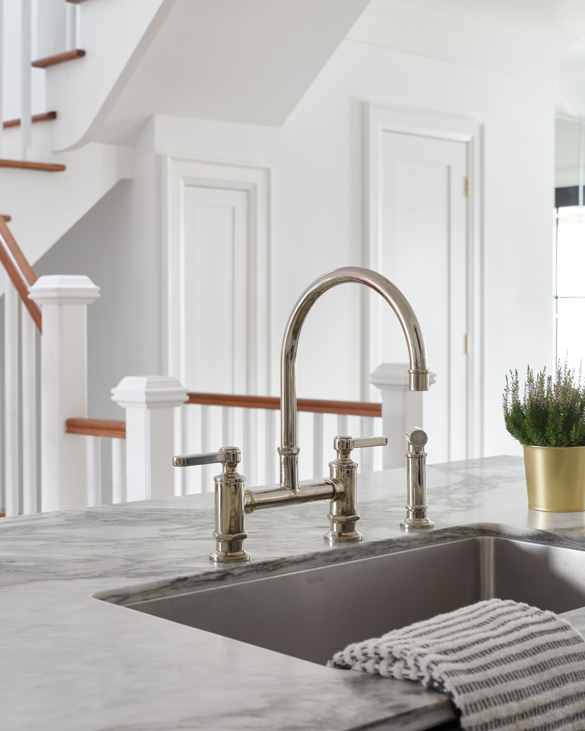 A kitchen sink with a faucet and stairs in the background