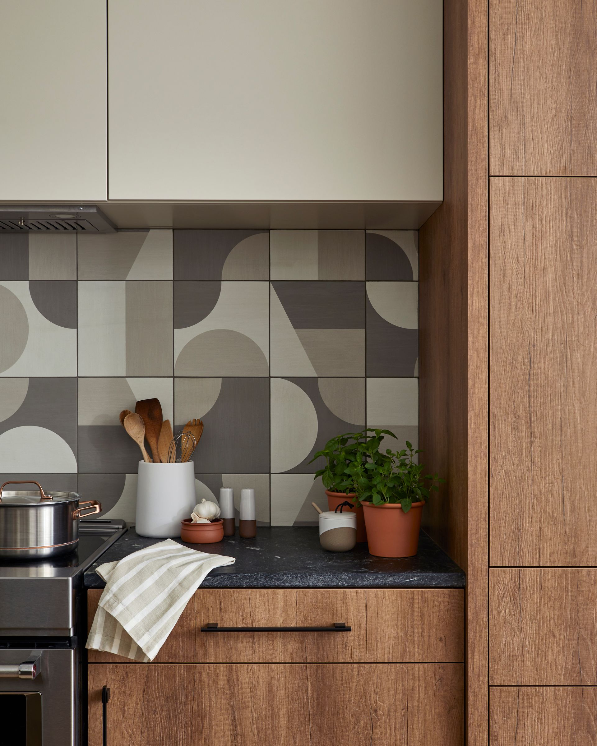 A kitchen with a pot on the stove and potted plants on the counter.