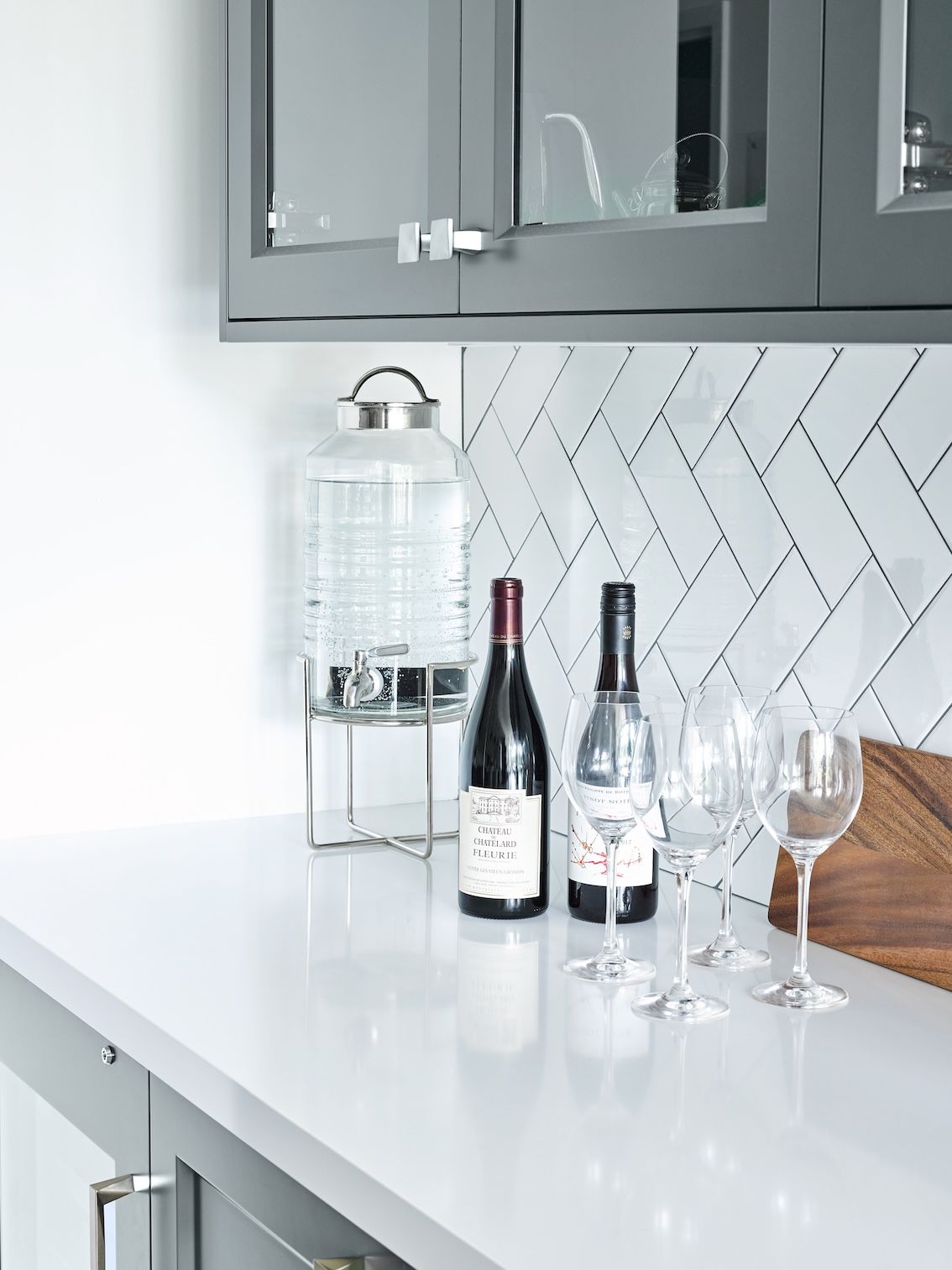 A kitchen counter with two bottles of wine and wine glasses on it.