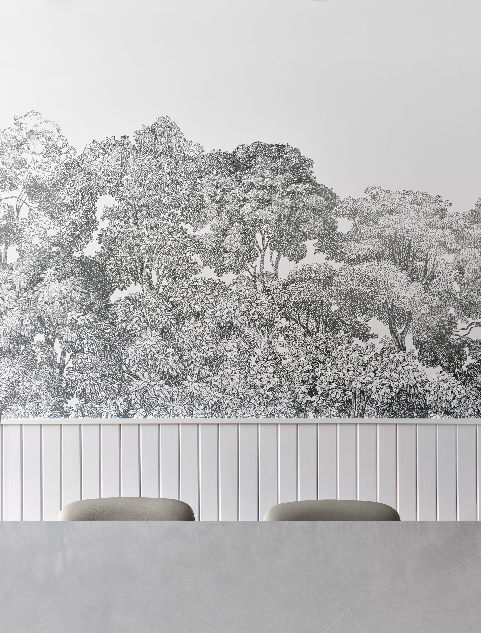 A black and white painting of trees on a wall above a table and chairs.