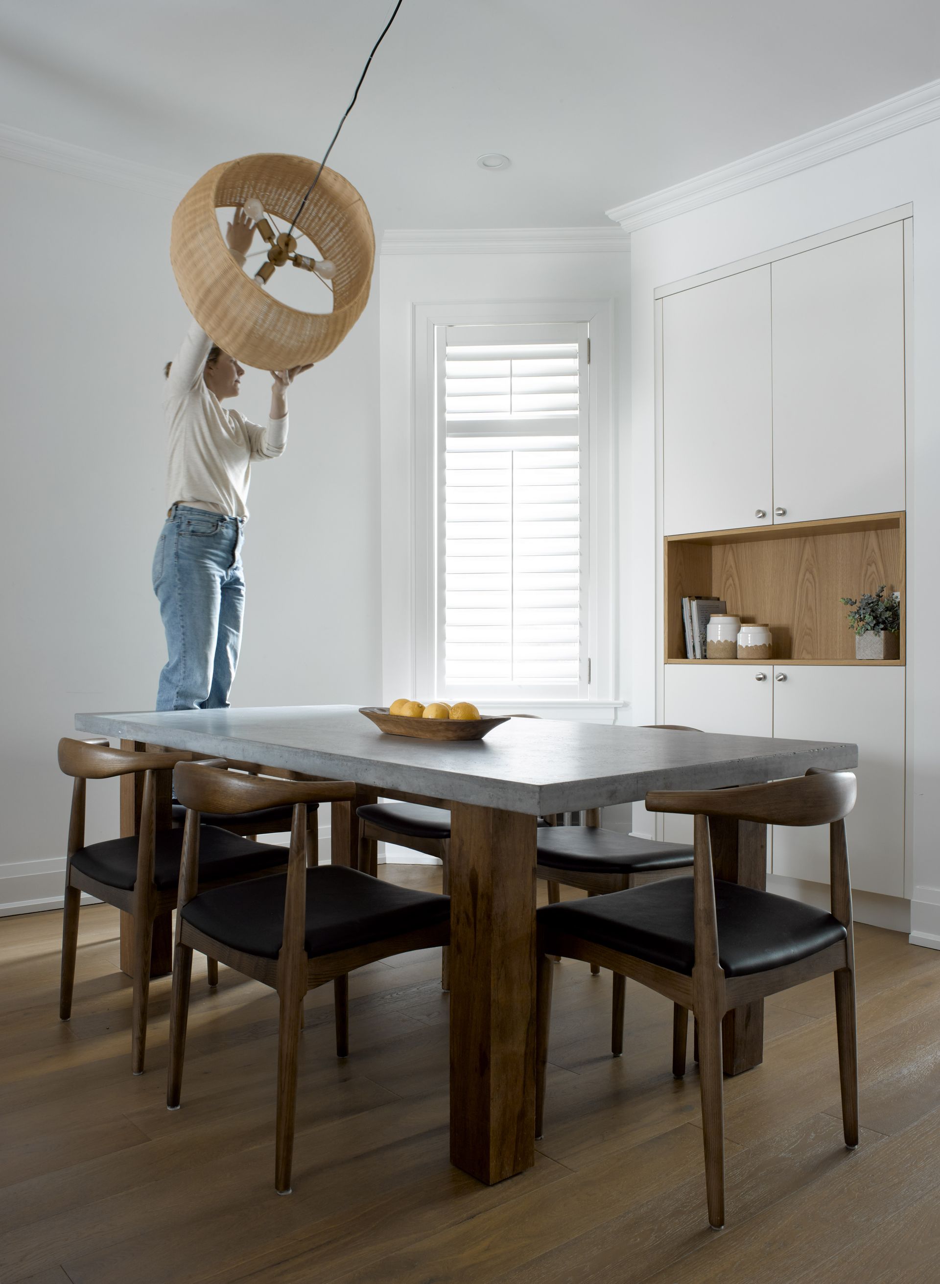 A man is standing on a table in a dining room holding a chandelier.