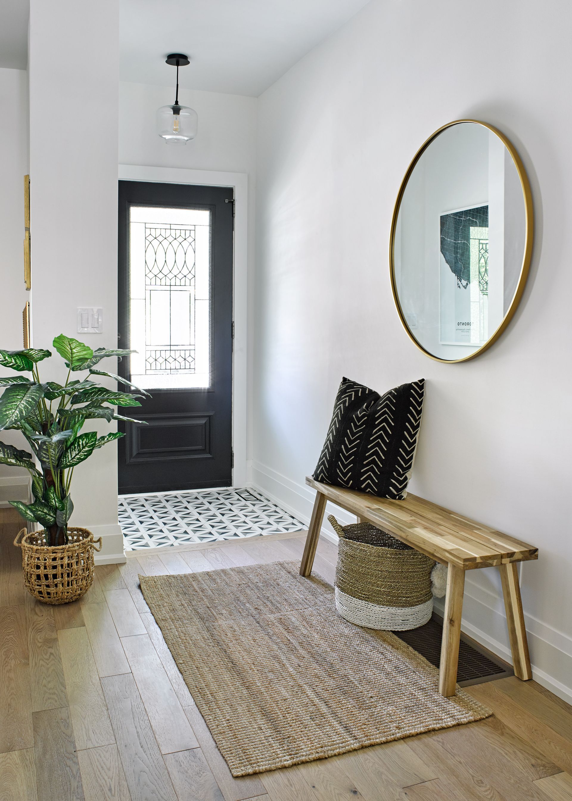 A hallway with a bench , rug , mirror and plant.