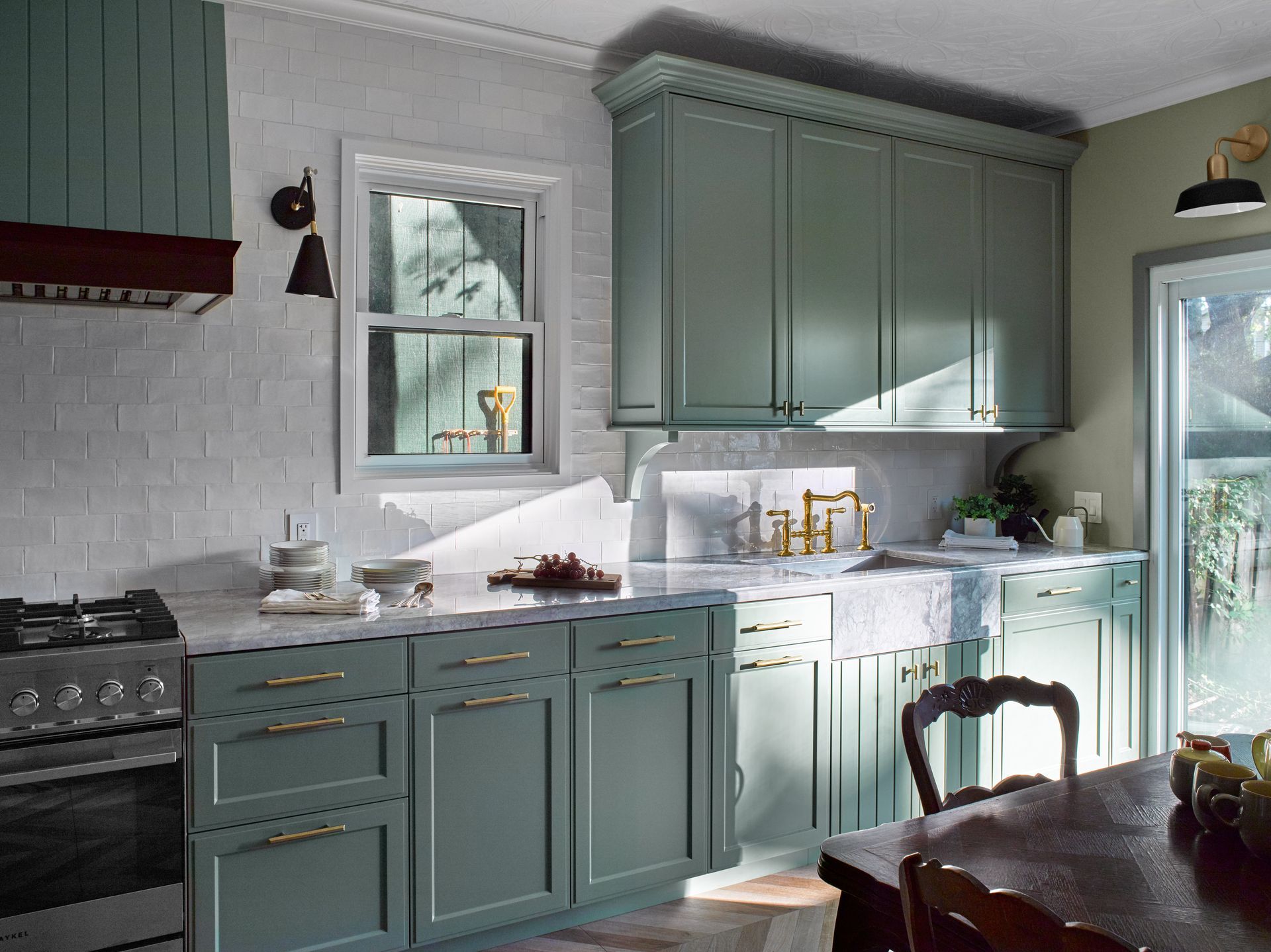 A kitchen with green cabinets , a stove , a sink , and a table.