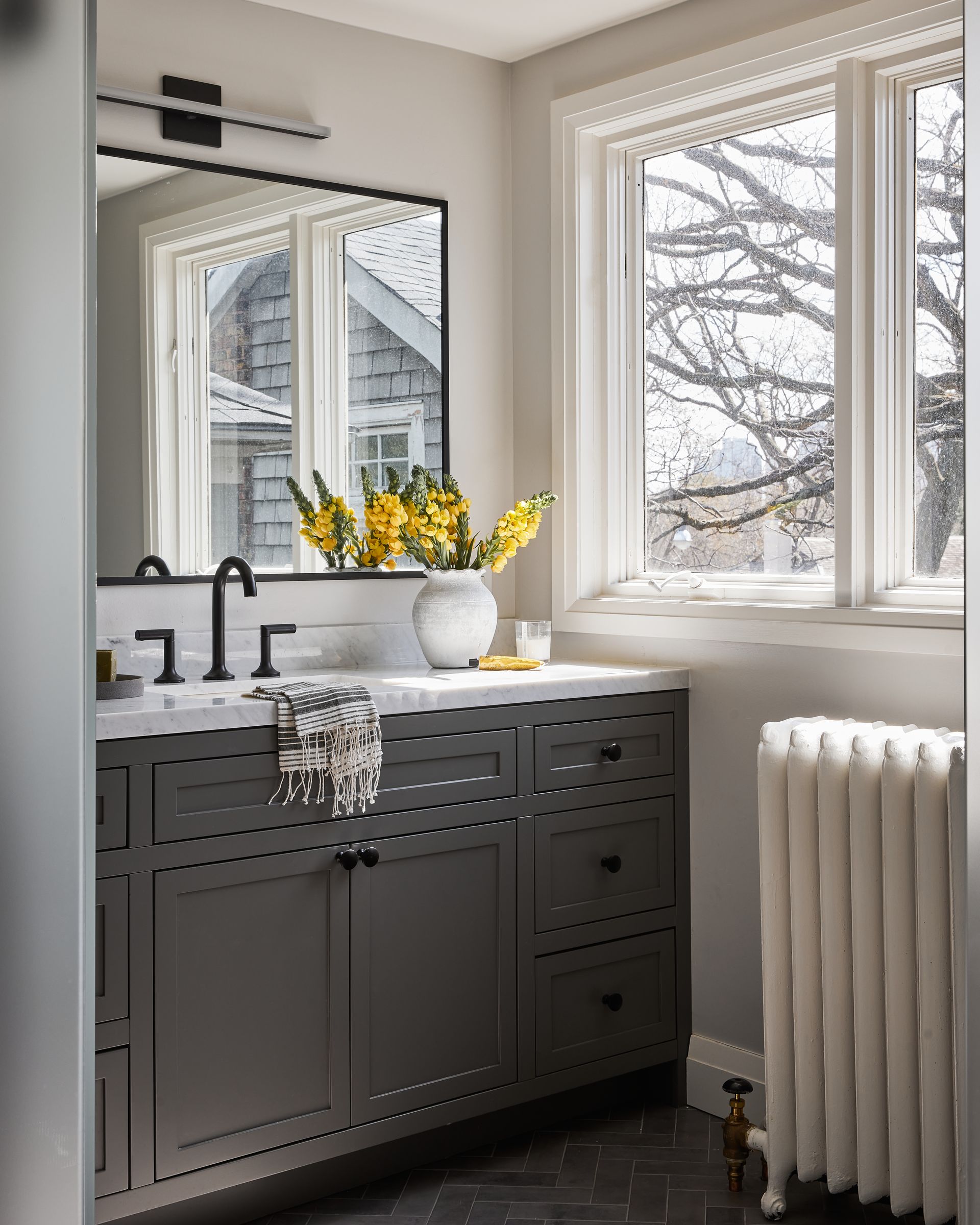 A bathroom with a sink , mirror , radiator and window.