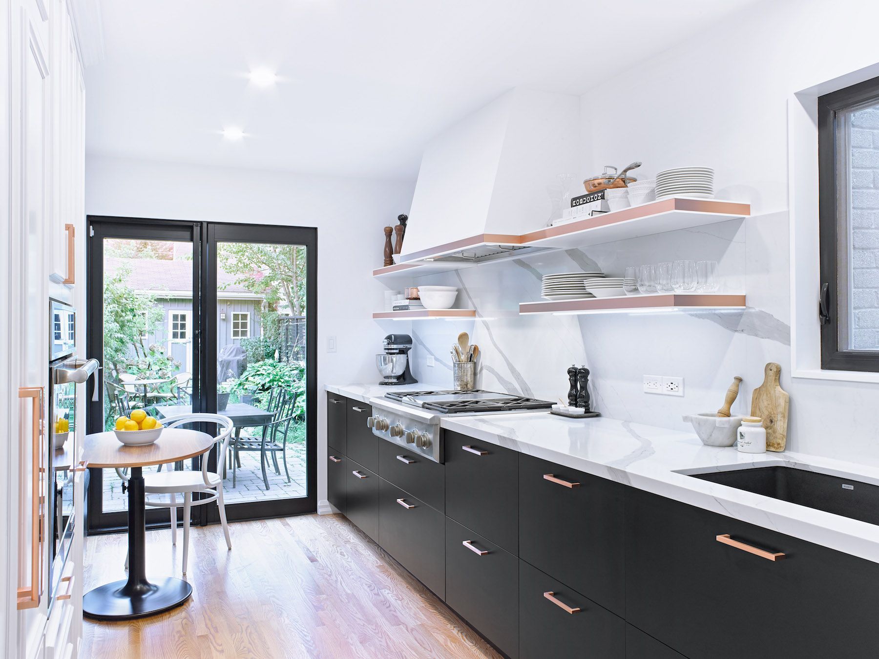 A kitchen with black cabinets , white counter tops , a stove and a table.
