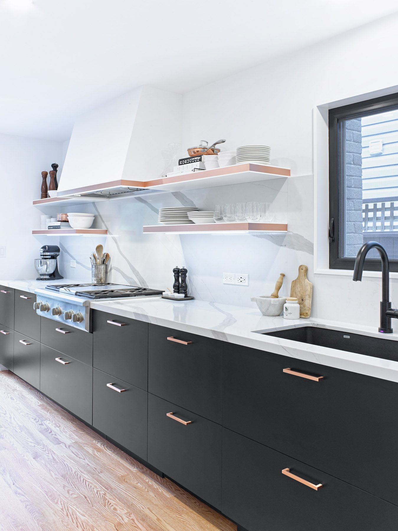 A kitchen with black cabinets , white counter tops , a sink and a stove.