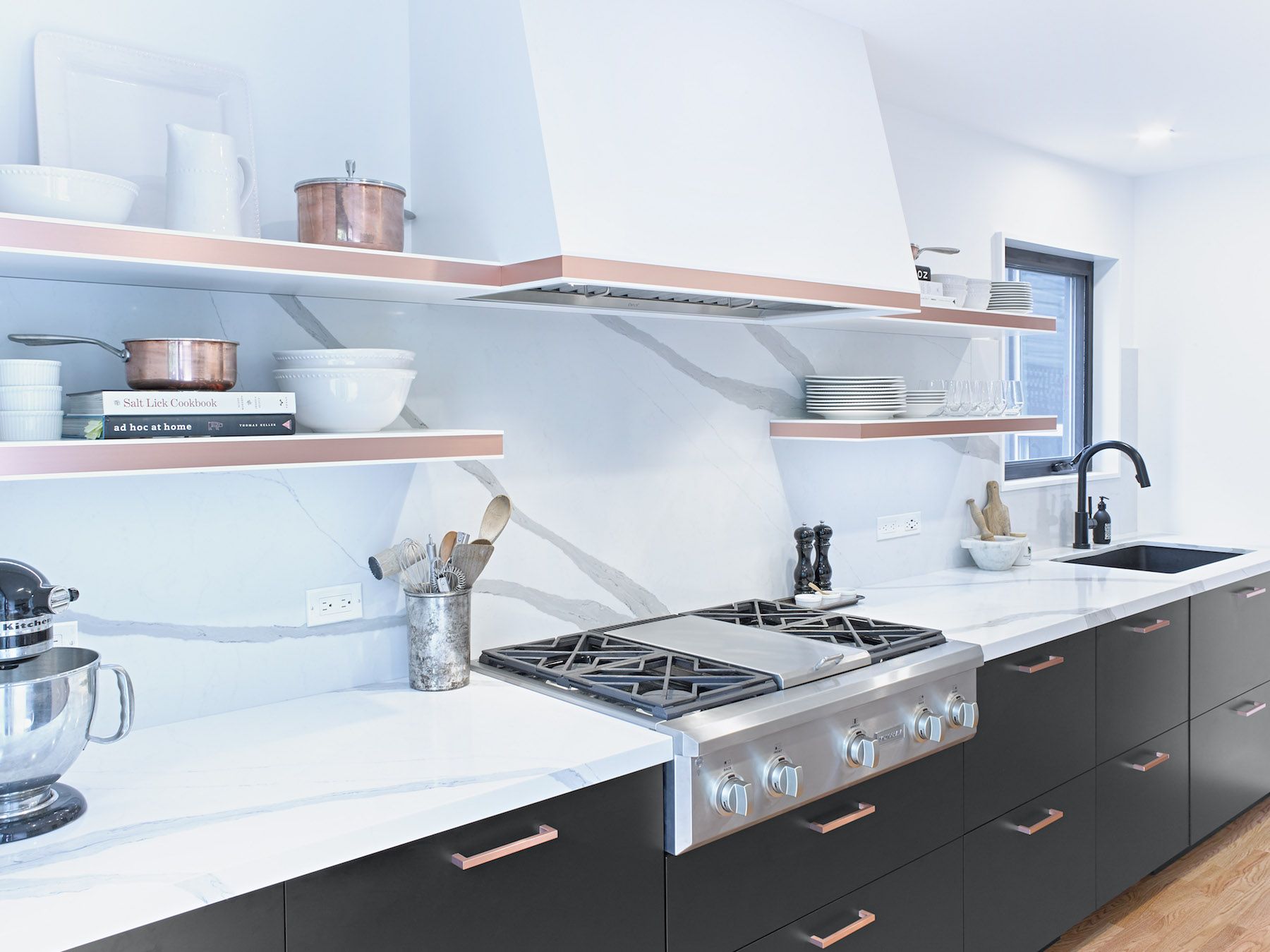 A kitchen with a stove top oven , sink , and shelves.