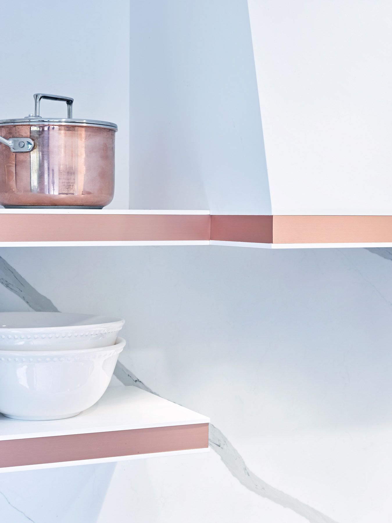 A copper pot sits on a shelf next to a white bowl