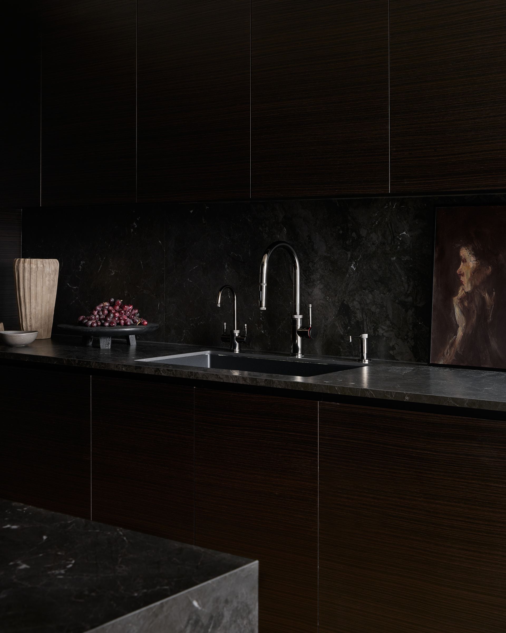 A dark kitchen with a sink and a painting on the wall.