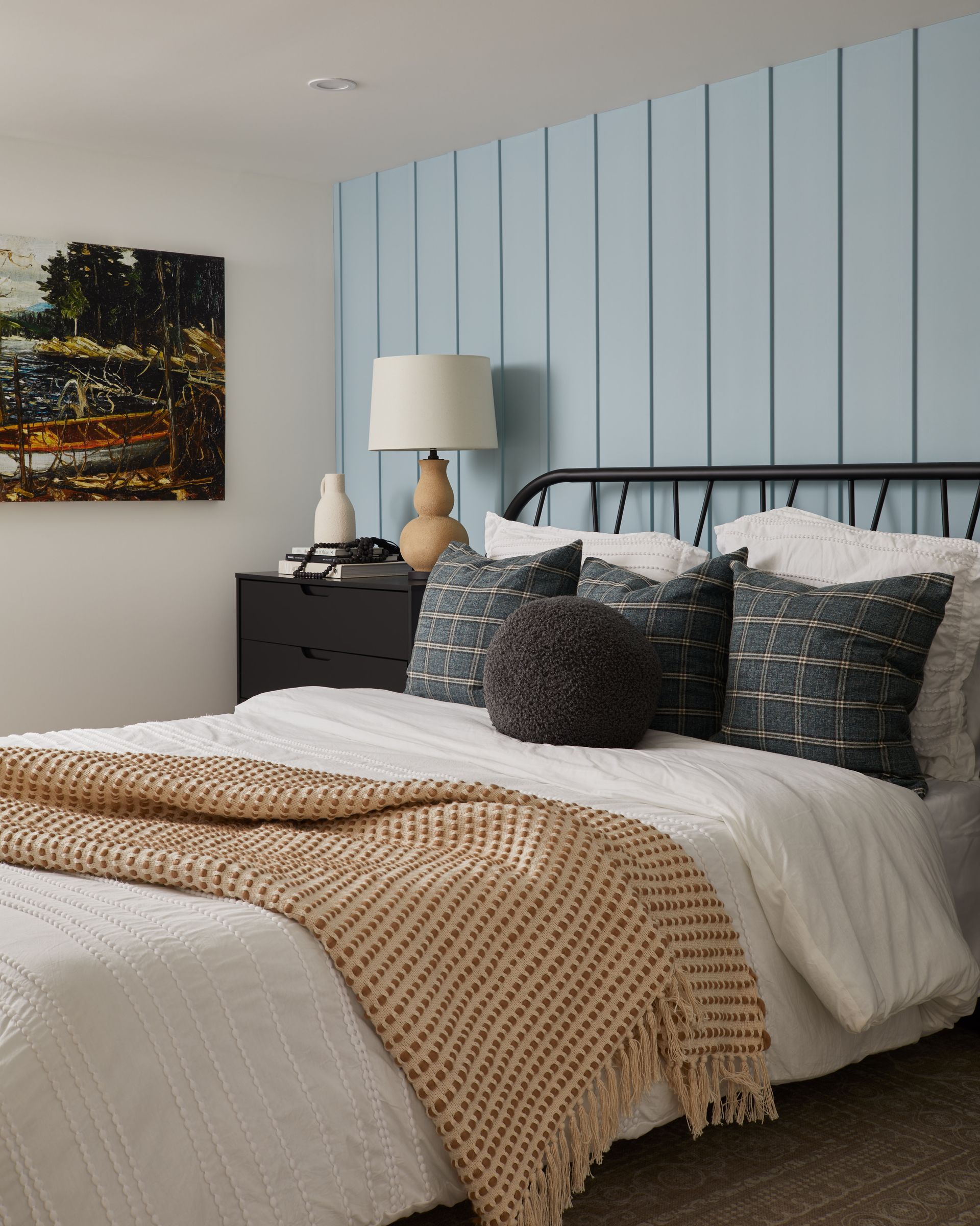 A bedroom with a bed , nightstand , lamp and painting on the wall.