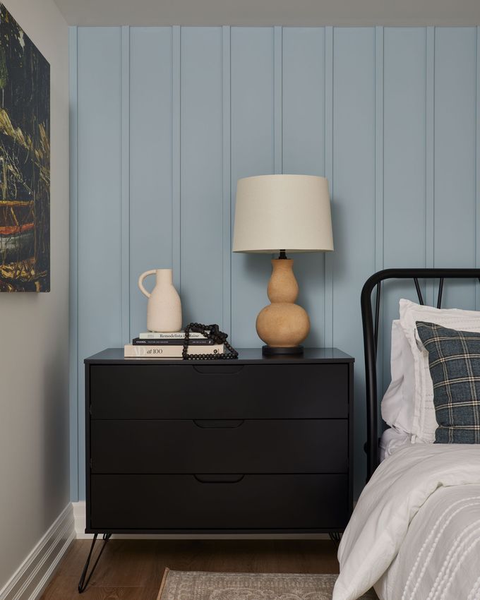 A bedroom with a bed , nightstand , lamp and dresser.