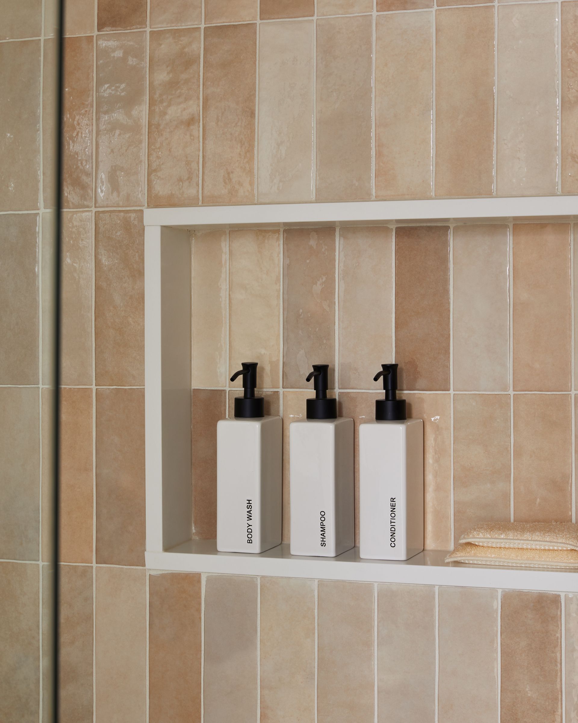 Three bottles of lotion are on a shelf in a bathroom