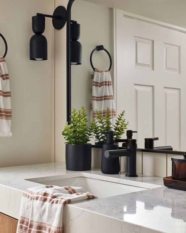 A bathroom with a sink , mirror , towels and plants.