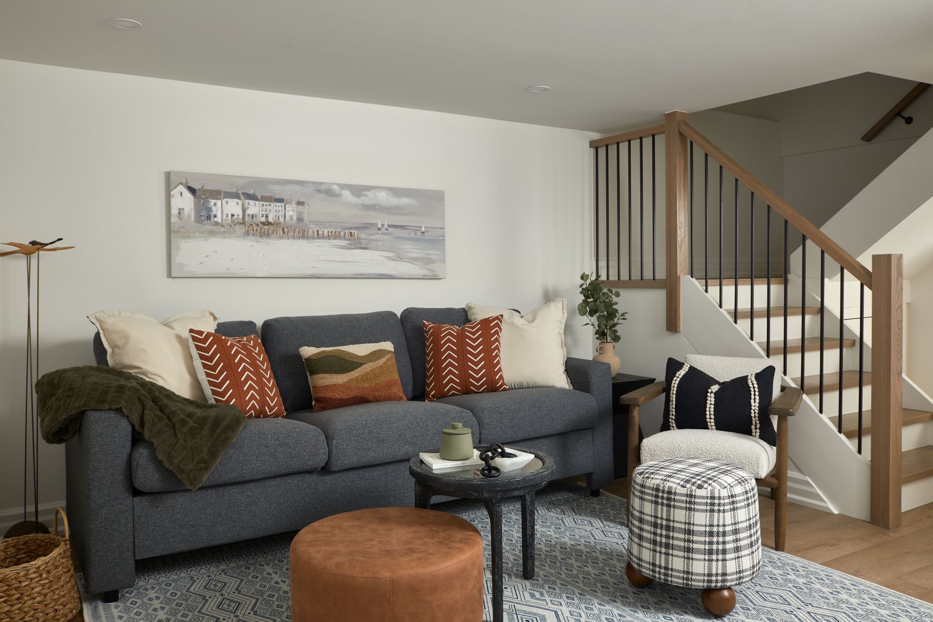 A living room with a couch , chairs , ottomans and stairs.