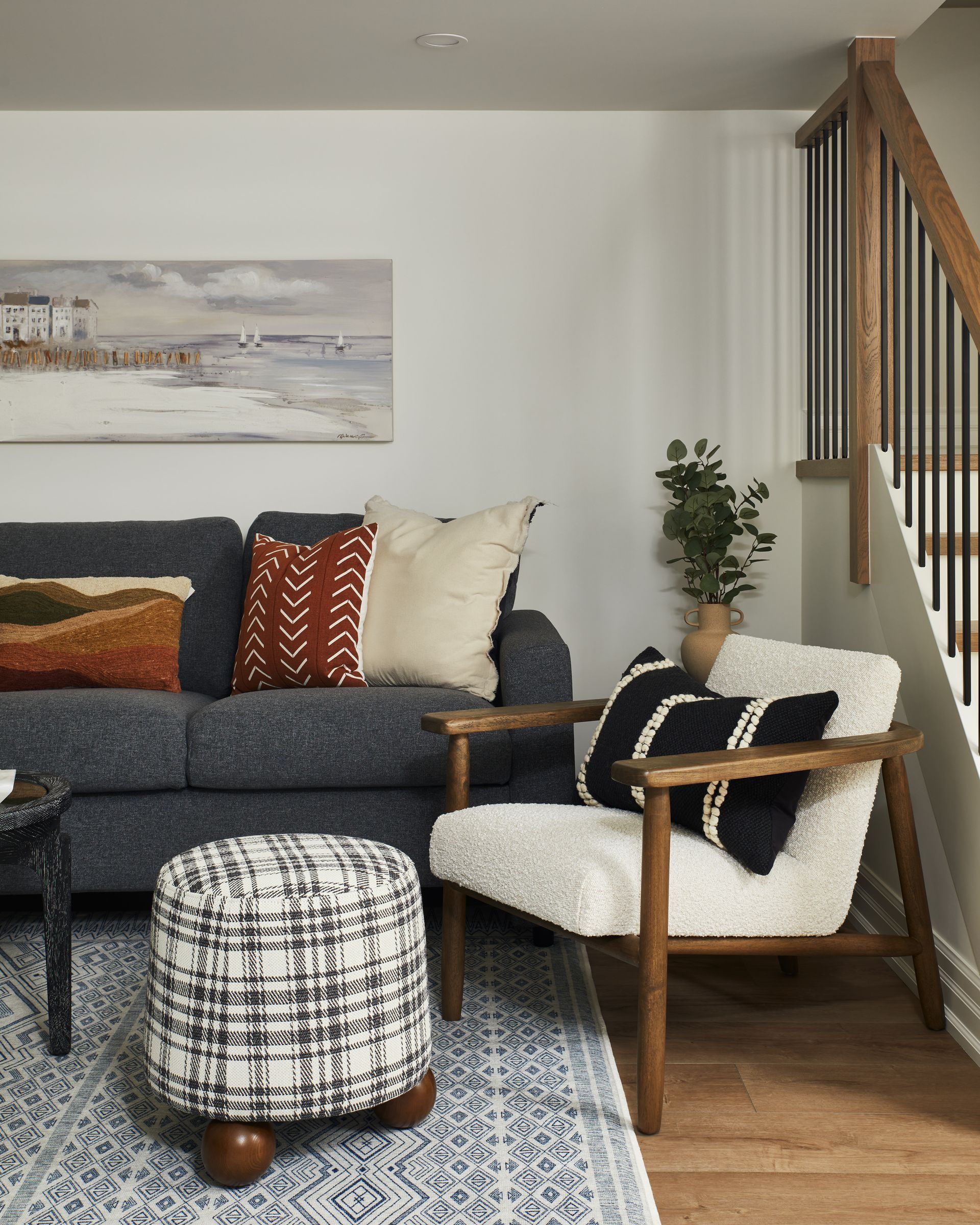 A living room with a couch , chair , ottoman and stairs.