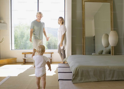 Three people standing in a bright bedroom by a large window, one child facing them in the foreground.