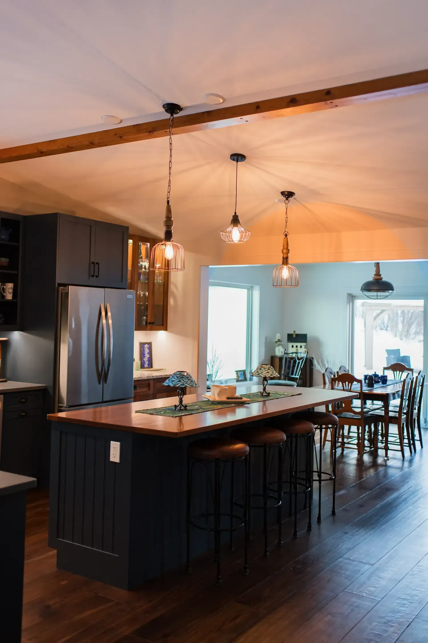 Modern kitchen with dark island, pendant lights, wood floors, and dining area in the background