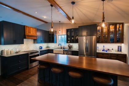 Modern kitchen with dark cabinets, stainless steel fridge, white backsplash, and a large wooden island