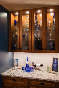 Wooden glass-front cabinets above a granite bathroom vanity with blue decor and mirror lights.
