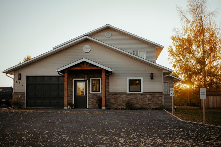Suburban house with a stone and tan exterior, dark garage door, and autumn trees at dusk