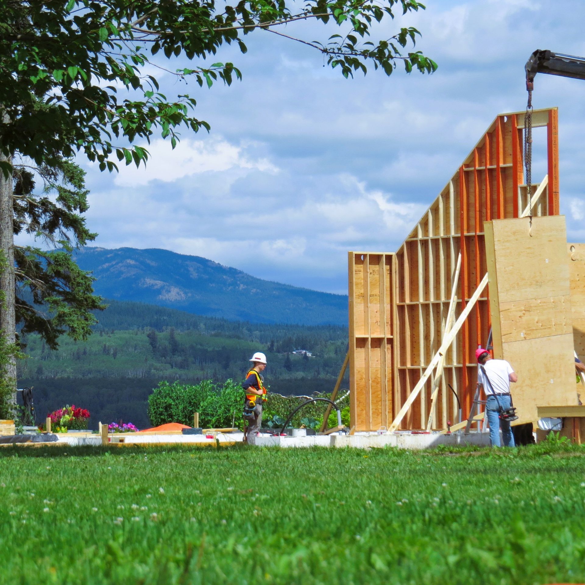 Construction workers building a wooden frame against a mountain backdrop under a cloudy sky