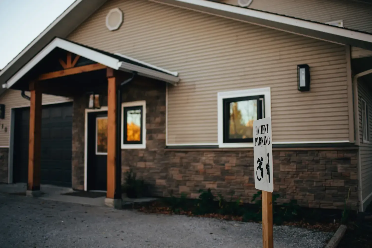 Single-story building with tan siding, stone base, and a posted sign outside at dusk