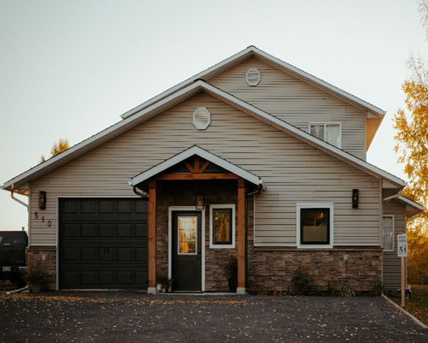Front view of a beige house with a single-car garage, stone accents, and a peaked roof.