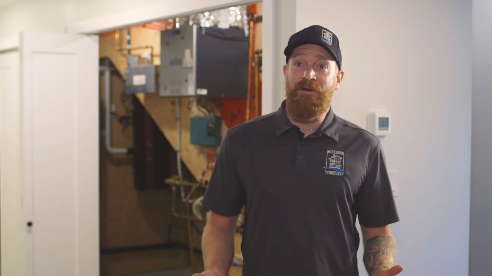 Man standing in a doorway to a utility room, wearing a black shirt and cap, with electrical equipment visible behind him.