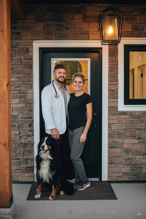 Two people and a dog standing at a brick building entrance under a lit lantern