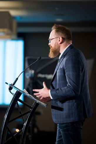 Man in blue suit speaking at a podium on a stage with a microphone