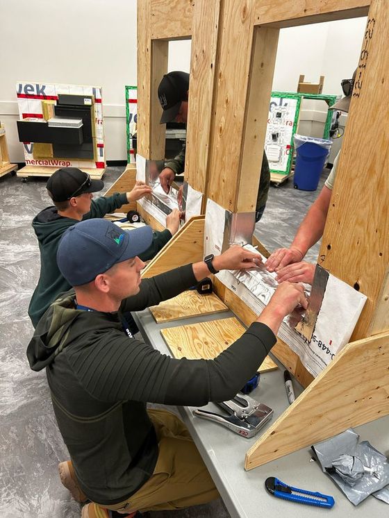 People assembling a wooden structure at a workbench in a workshop.