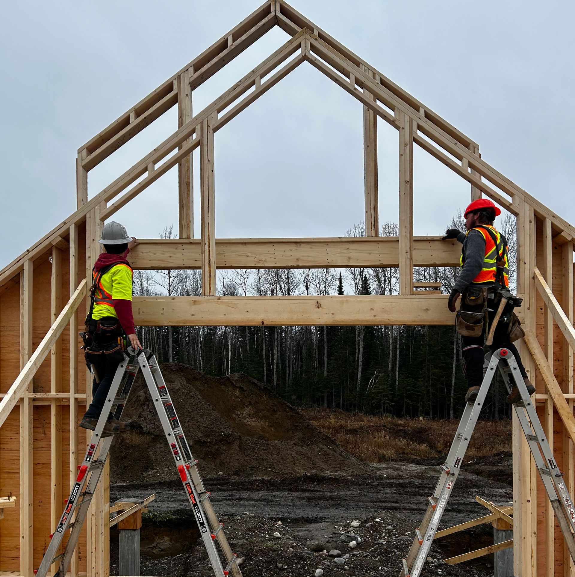 Two construction workers on ladders framing a wooden house roof against a cloudy sky