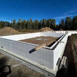 Concrete foundation walls at a construction site with dirt fill and a blue sky background