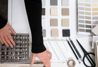 Hands arranging fabric samples beside color swatches, scissors, and design tools on a desk.