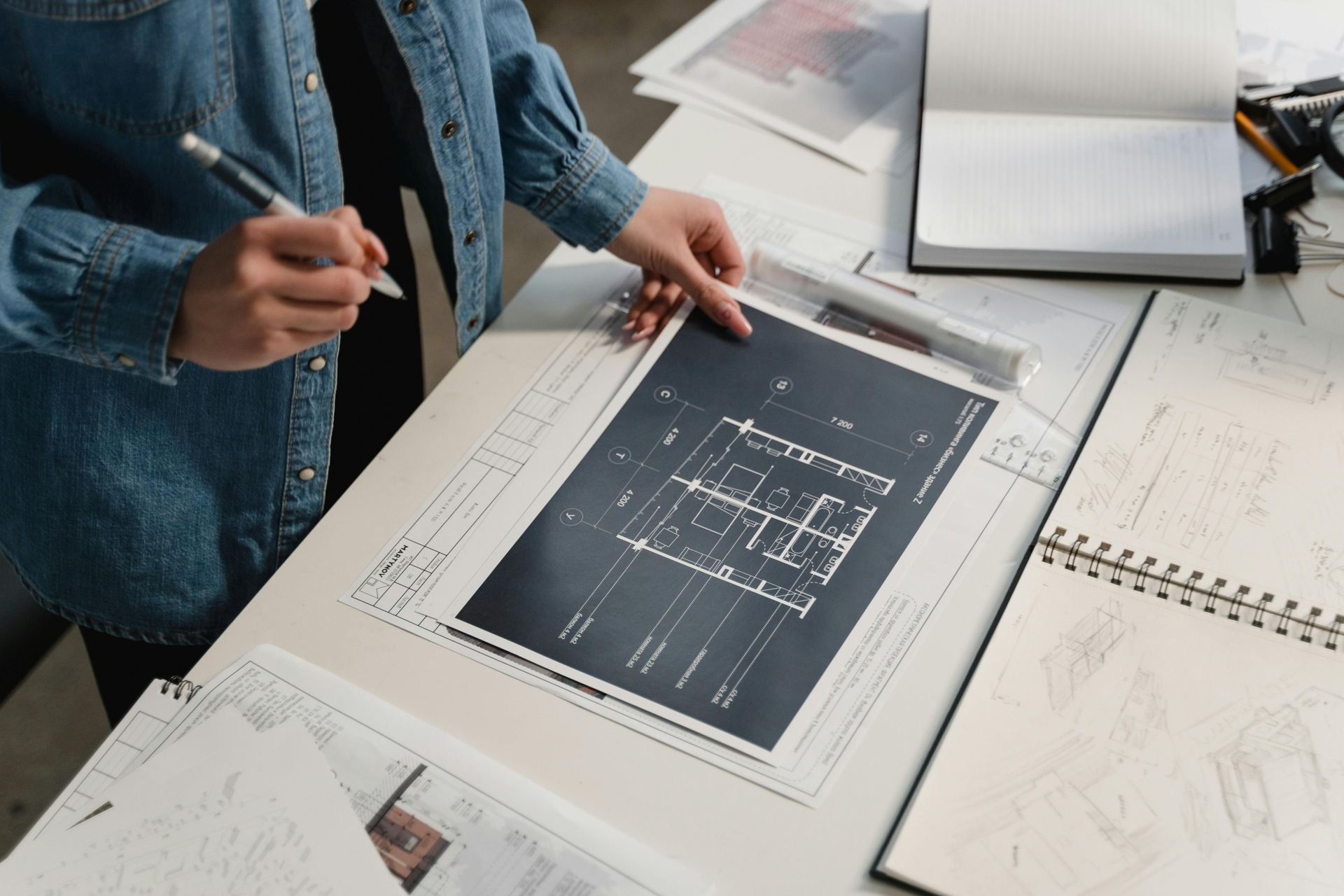 Person reviewing a large architectural blueprint on a desk with sketches and a laptop nearby