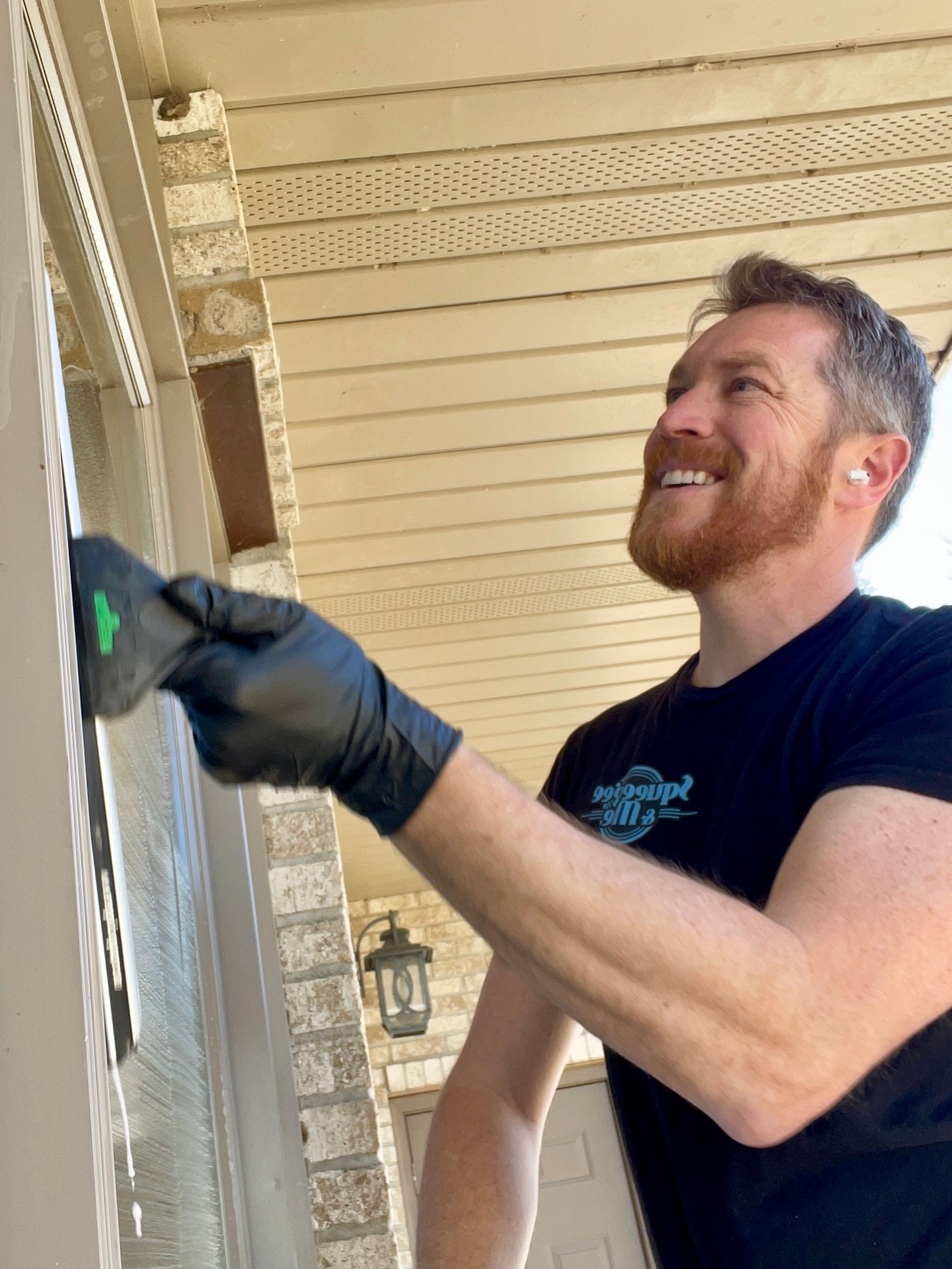 A man wearing black gloves is cleaning a door with a spatula.