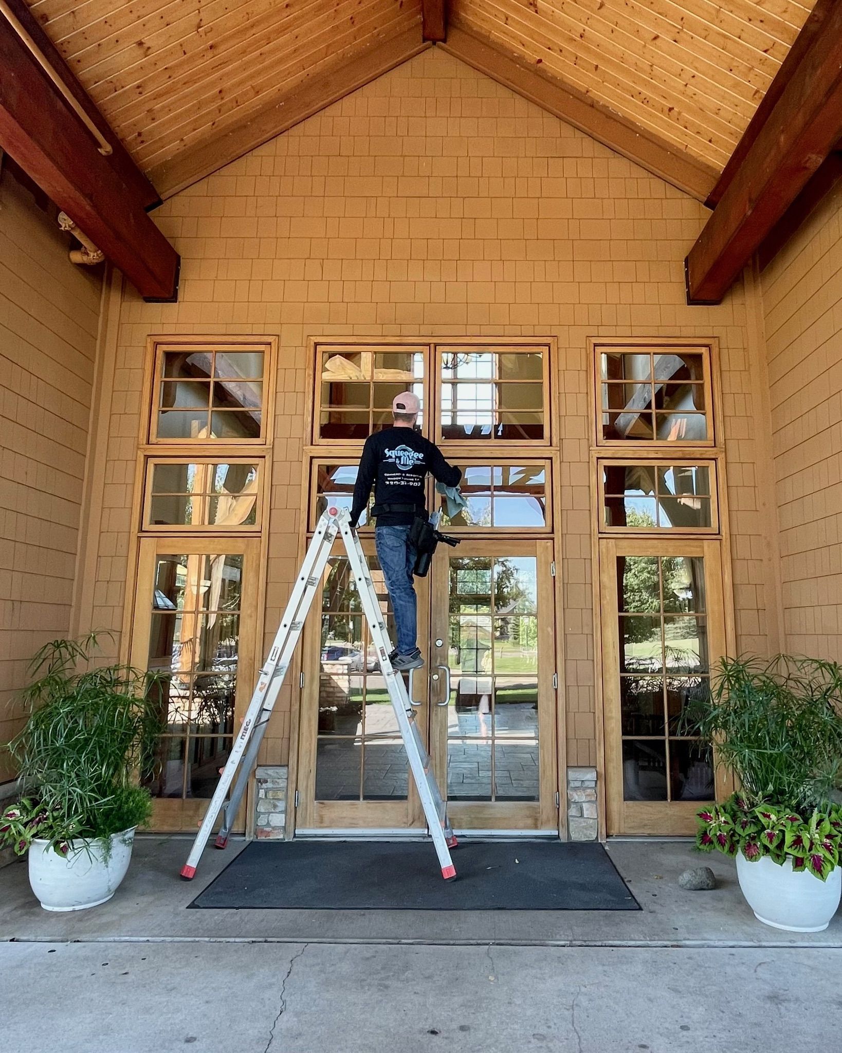 A man is standing on a ladder cleaning the windows of a building.