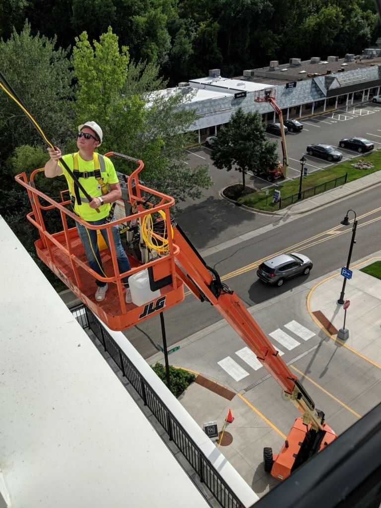 A man is standing in a bucket on top of a building.