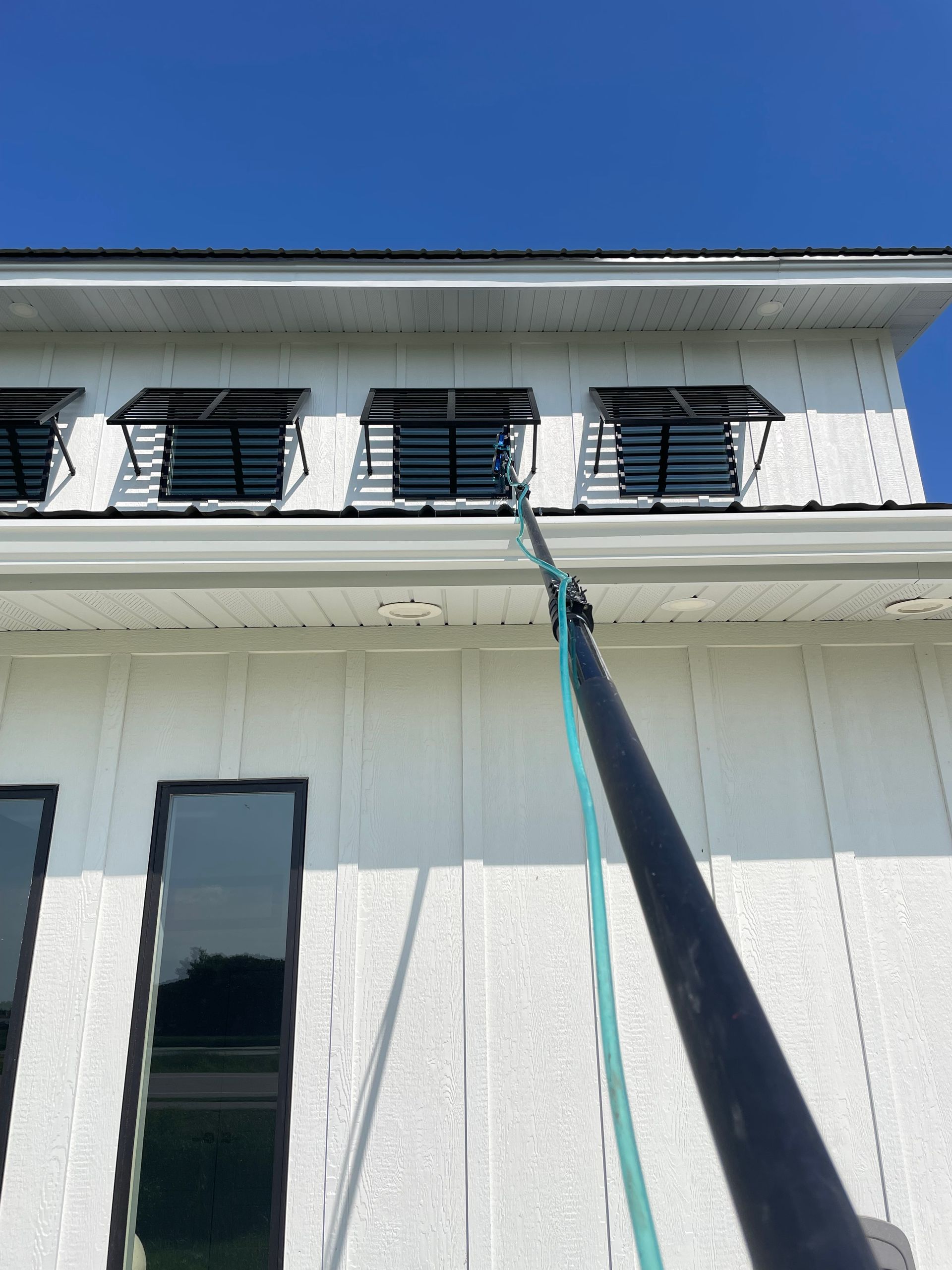 A person is cleaning the windows of a white building with a hose.