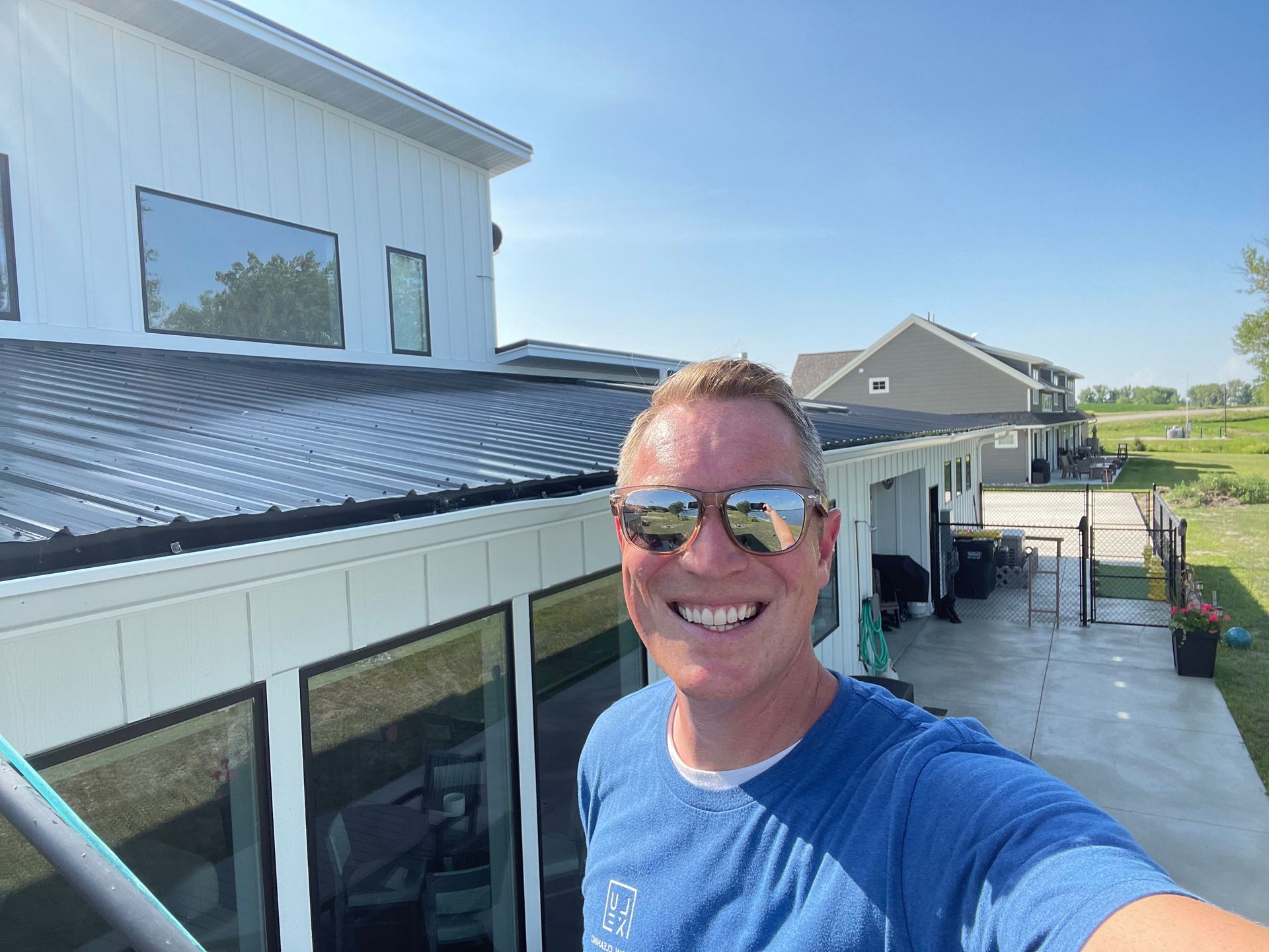 A man wearing sunglasses is taking a selfie in front of a house.