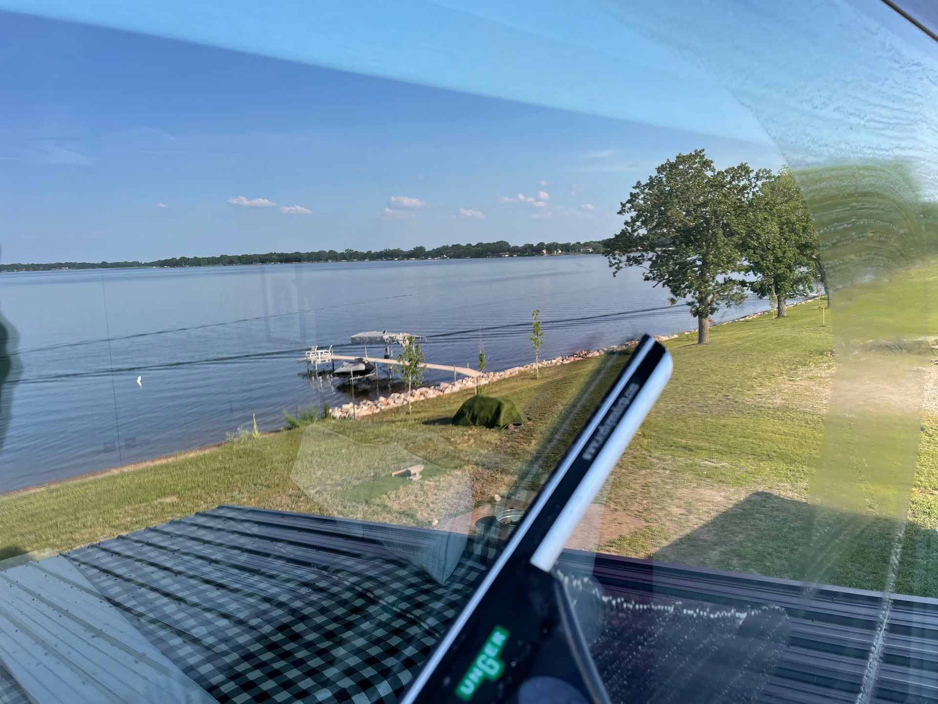 A cell phone is sitting on a windshield next to a lake.