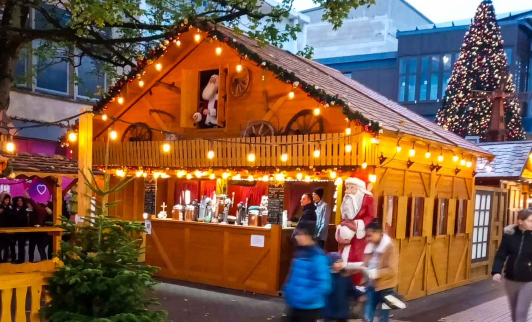 A group of people are standing outside of a wooden house decorated for christmas