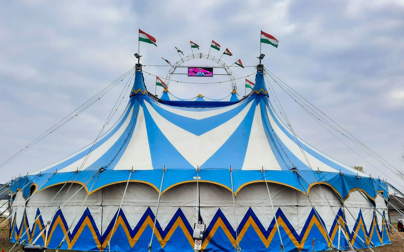 A blue and white circus tent with flags hanging from it