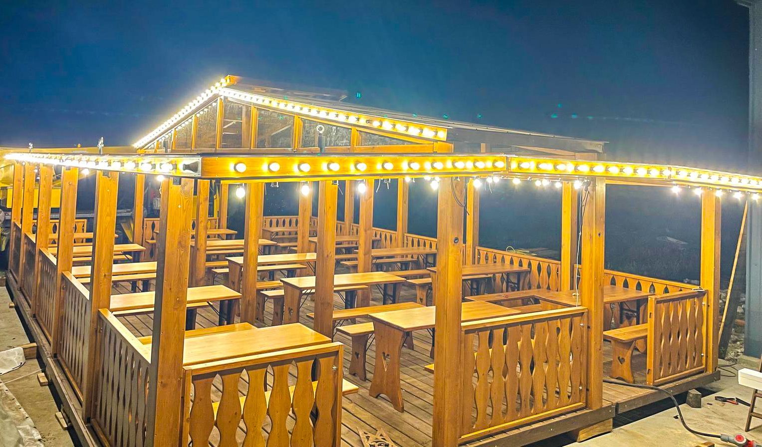 A wooden deck with tables and benches is lit up at night.